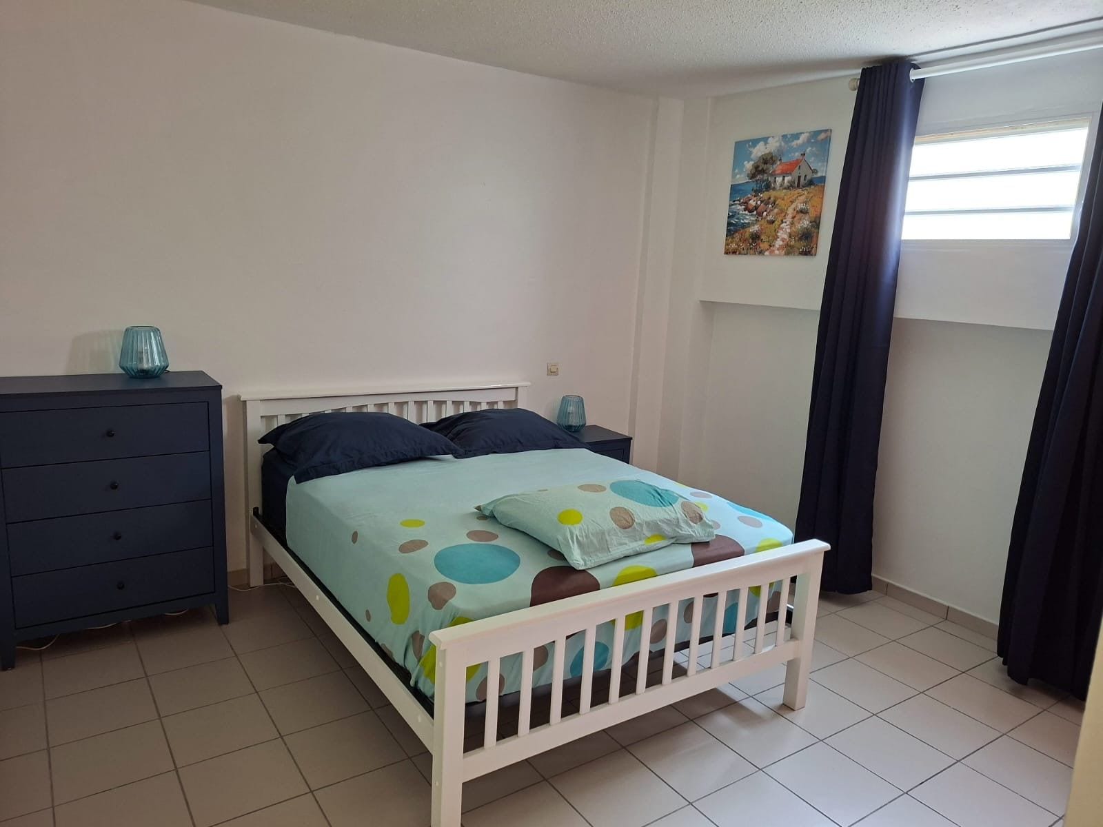 Un dormitorio con cama, cómoda, mesita de noche y un cuadro en la pared.