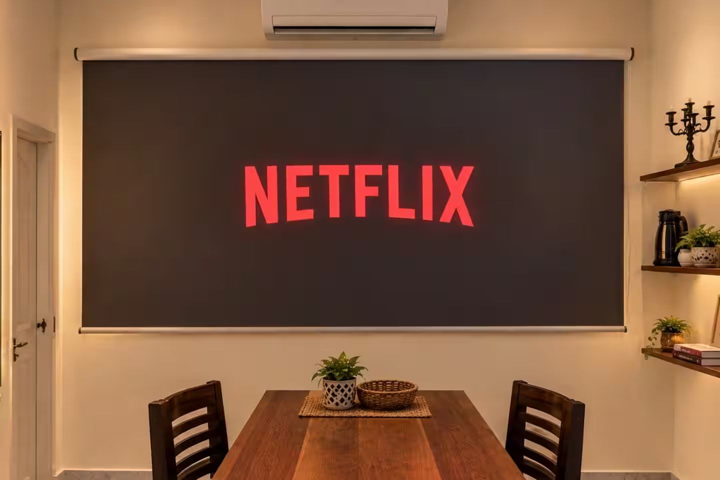 Una habitación con una pizarra grande que muestra 'NETFLIX' en letras rojas, una mesa de comedor de madera con sillas, una planta en maceta y un estante con objetos decorativos.