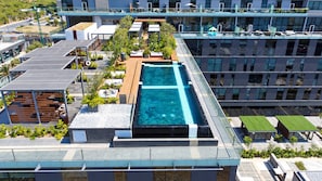 Piscina en la azotea con agua cristalina y azul, rodeada por una terraza de madera y plantas en macetas.