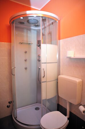Cabina de ducha con paredes de vidrio y un inodoro a la derecha.