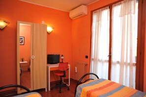 Una habitación con paredes anaranjadas, un escritorio con computadora, dos sillas, una cama con colcha a rayas y una ventana con cortinas.