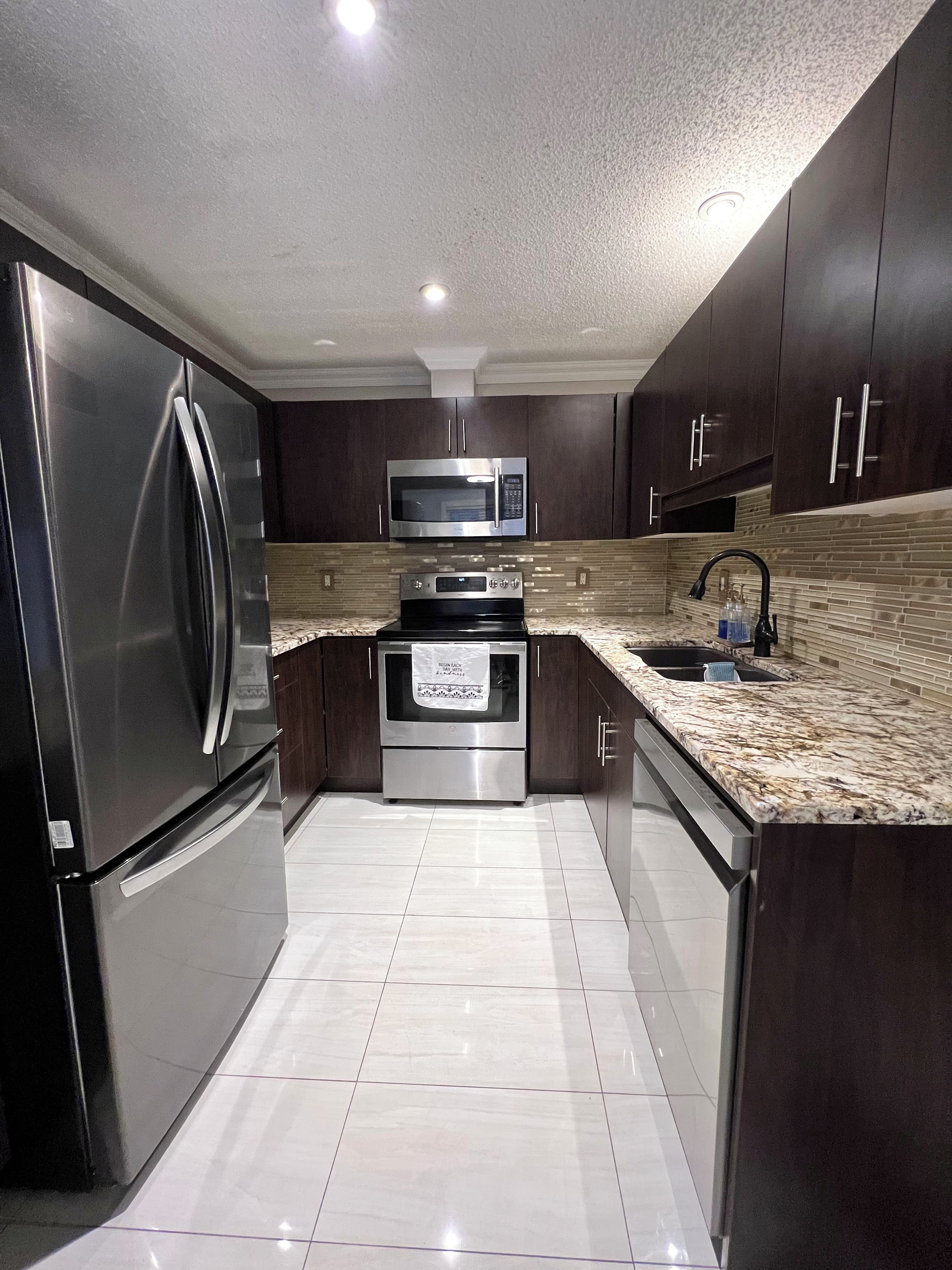 A modern kitchen with stainless steel appliances, dark wooden cabinets, and a tiled floor.