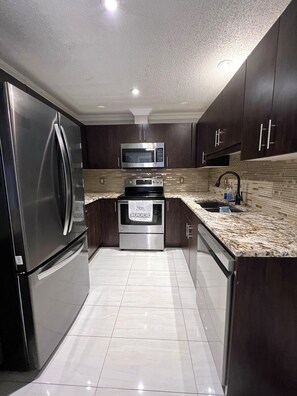 A modern kitchen with stainless steel appliances, dark wooden cabinets, and a tiled floor. - Pristine Spacious for Groups in Yeg|4mins to Wem (Edmonton)