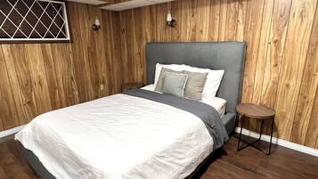 A bedroom with a wooden paneled wall, a bed with a grey headboard, and a small round table beside it.