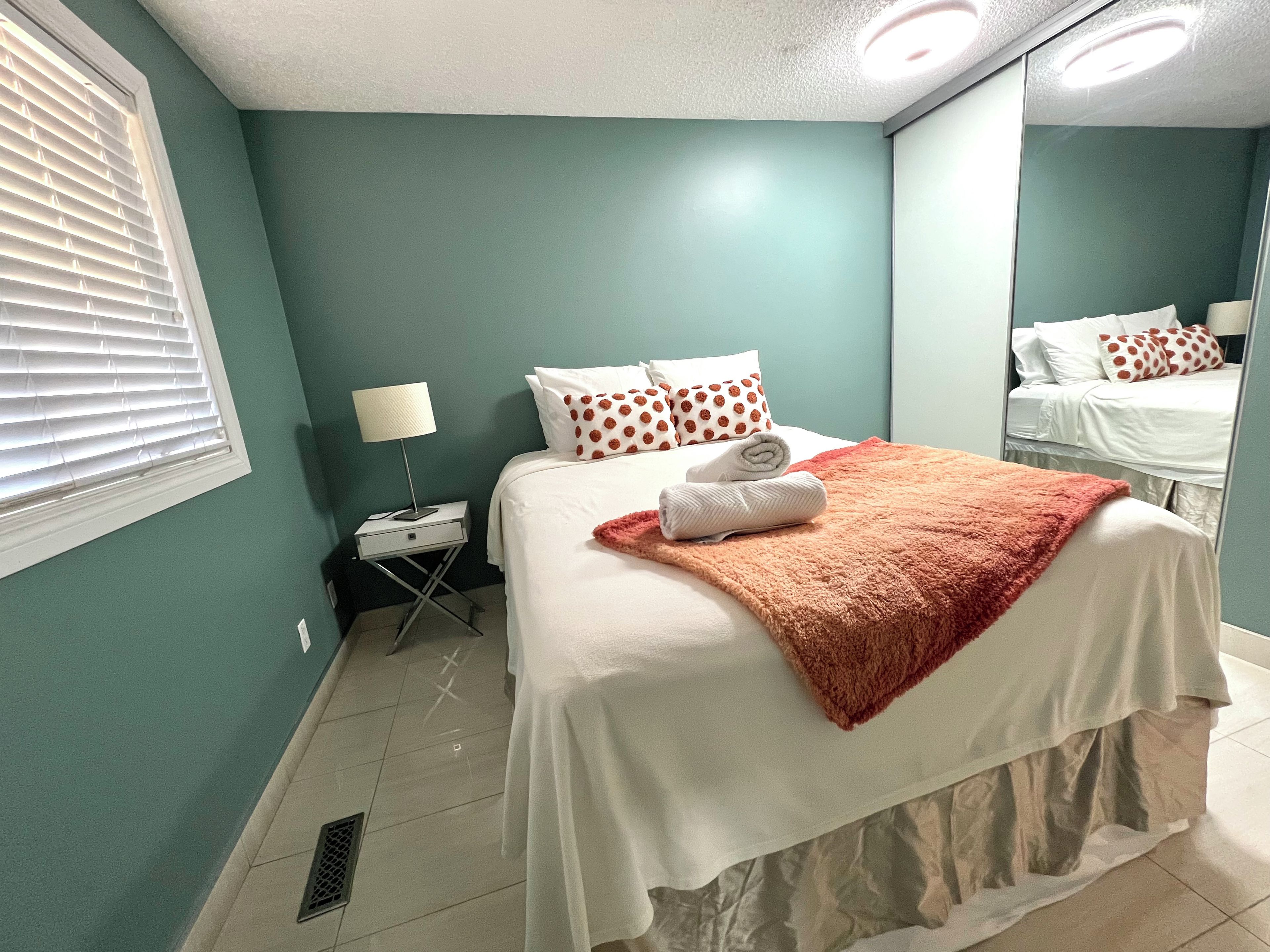 A hotel room with a bed, a nightstand, a lamp, and a mirror.