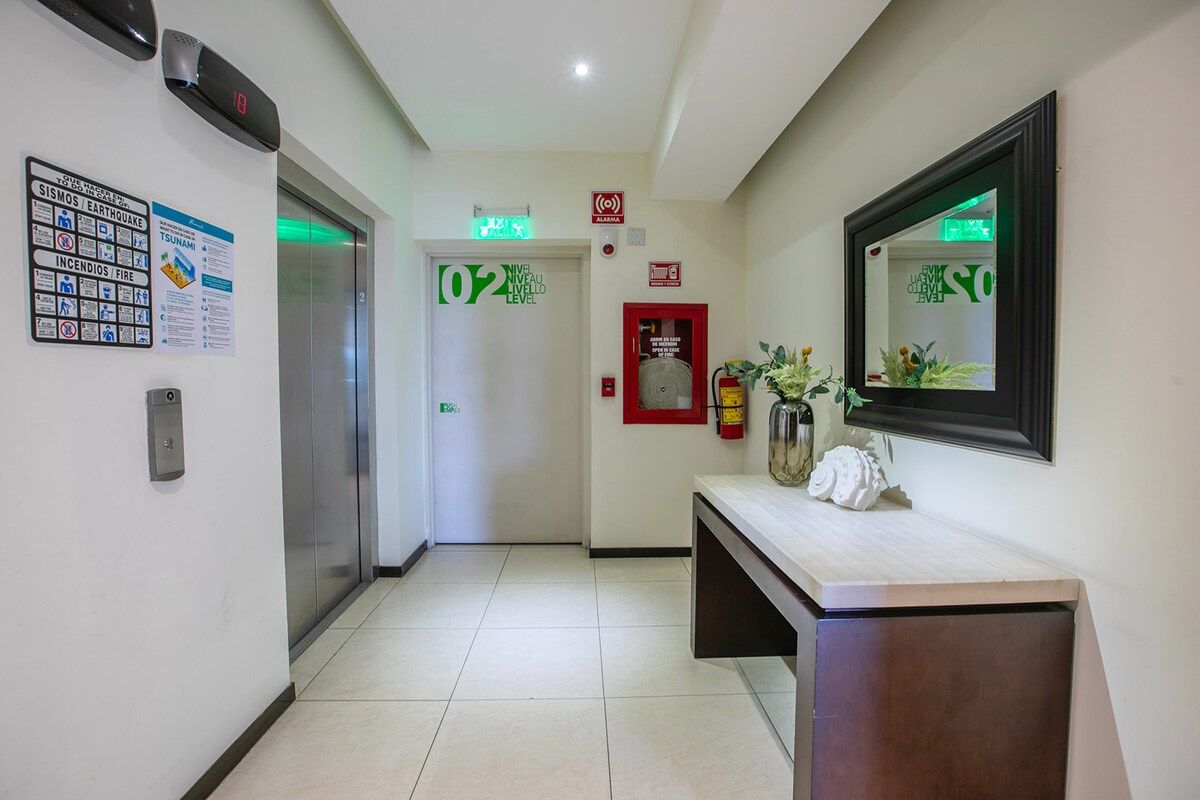 A hotel lobby with an elevator, a reception desk, and emergency exit signs.