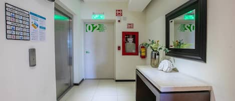 A hotel lobby with an elevator, a reception desk, and emergency exit signs.