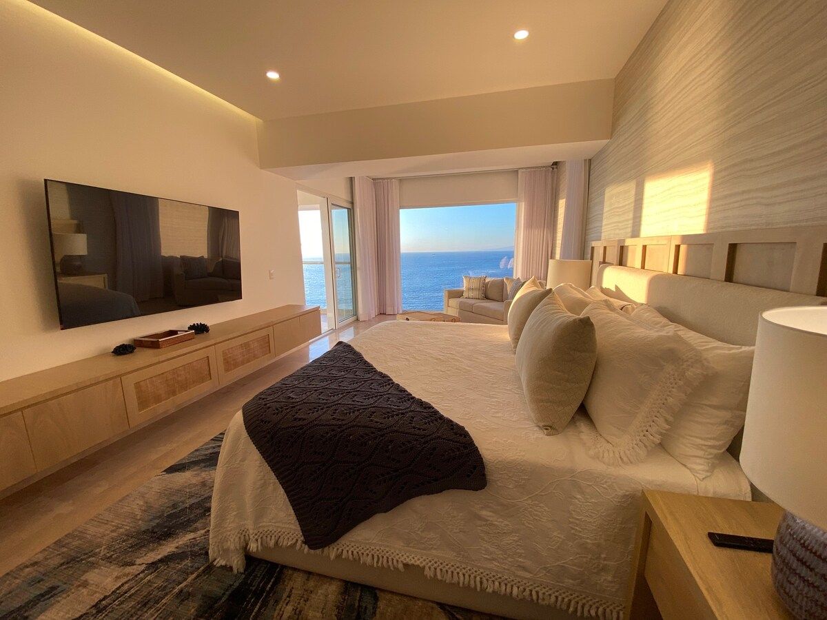 A spacious bedroom with a large bed, a flat-screen TV, a view of the sea, and a modern design.