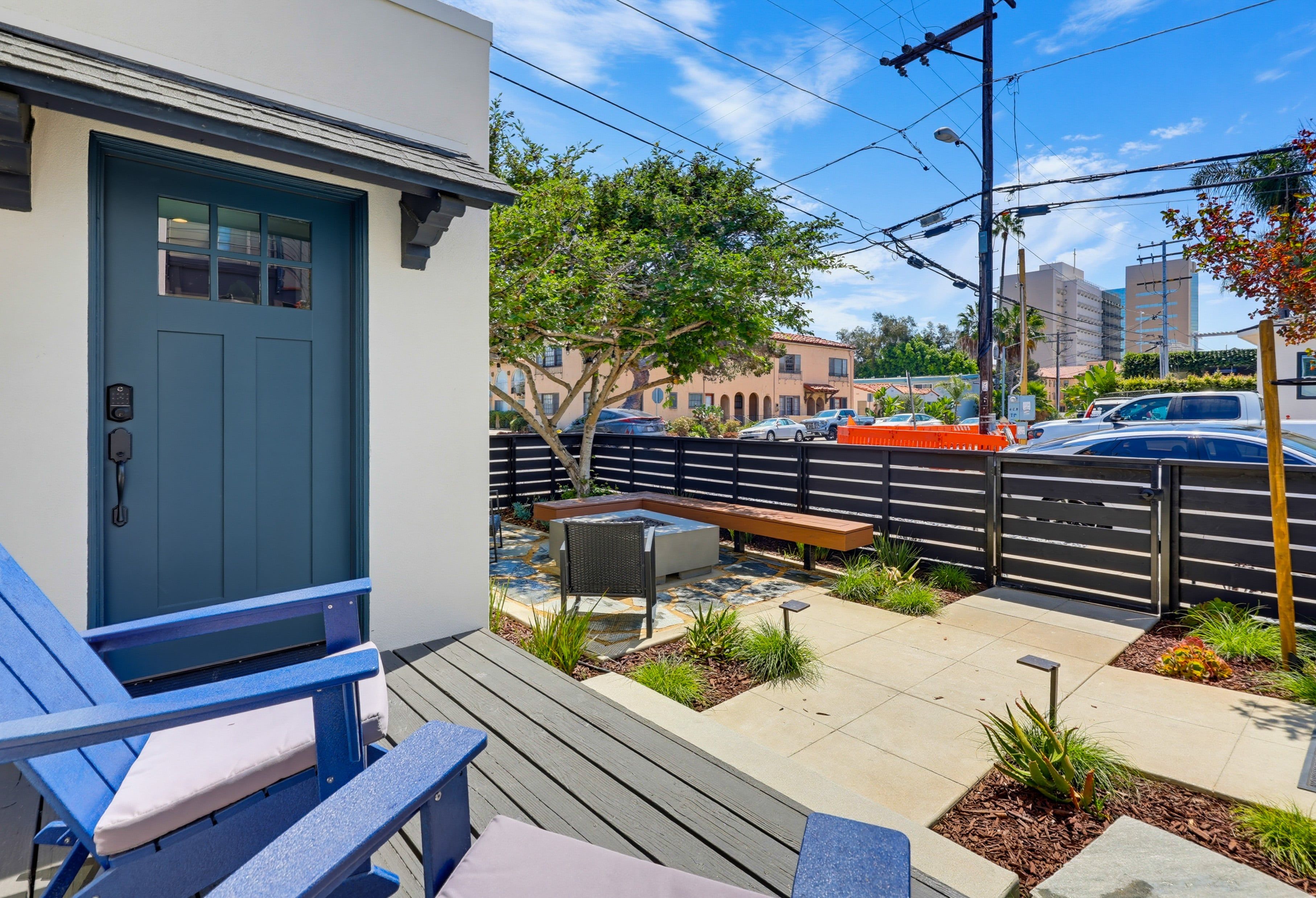 Une maison moderne avec une porte bleue, une terrasse avec des chaises bleues et un jardin clôturé.