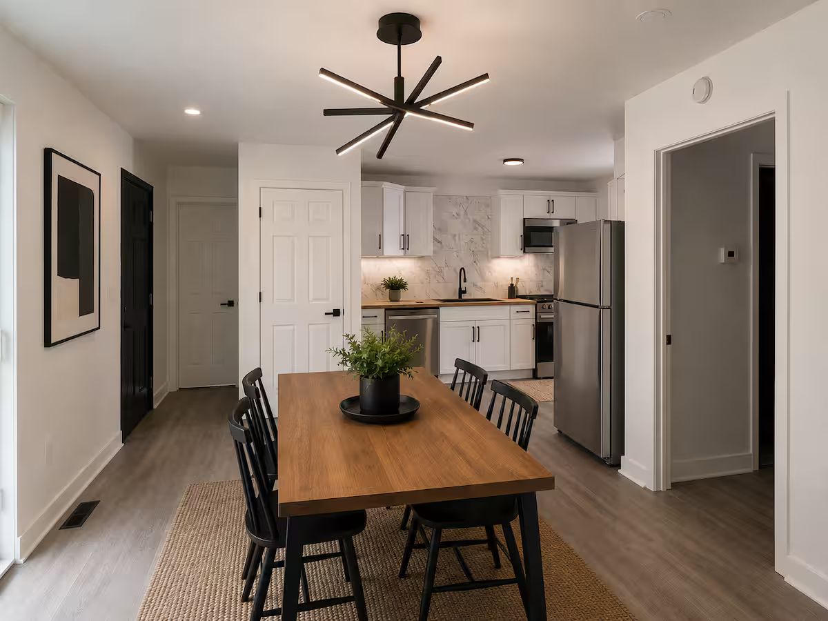 A modern kitchen with white cabinets, stainless steel appliances, and a wooden dining table with chairs.