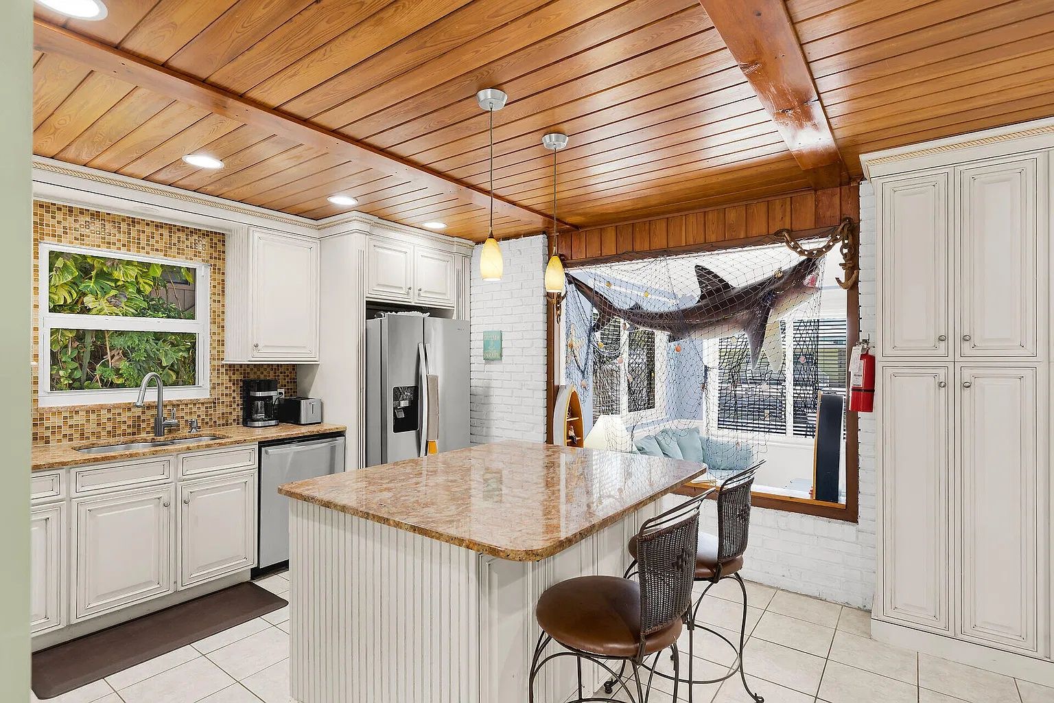 A kitchen with white cabinetry, a central island with bar stools, a hammock, and a view through a window.