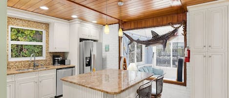 A kitchen with white cabinetry, a central island with bar stools, a hammock, and a view through a window.