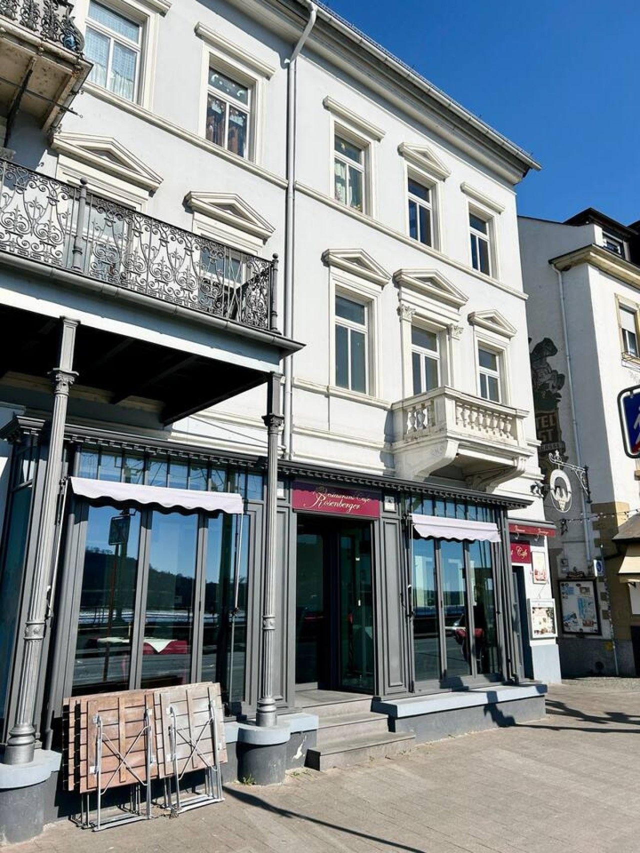A building with a balcony, large windows, and a storefront with a sign.