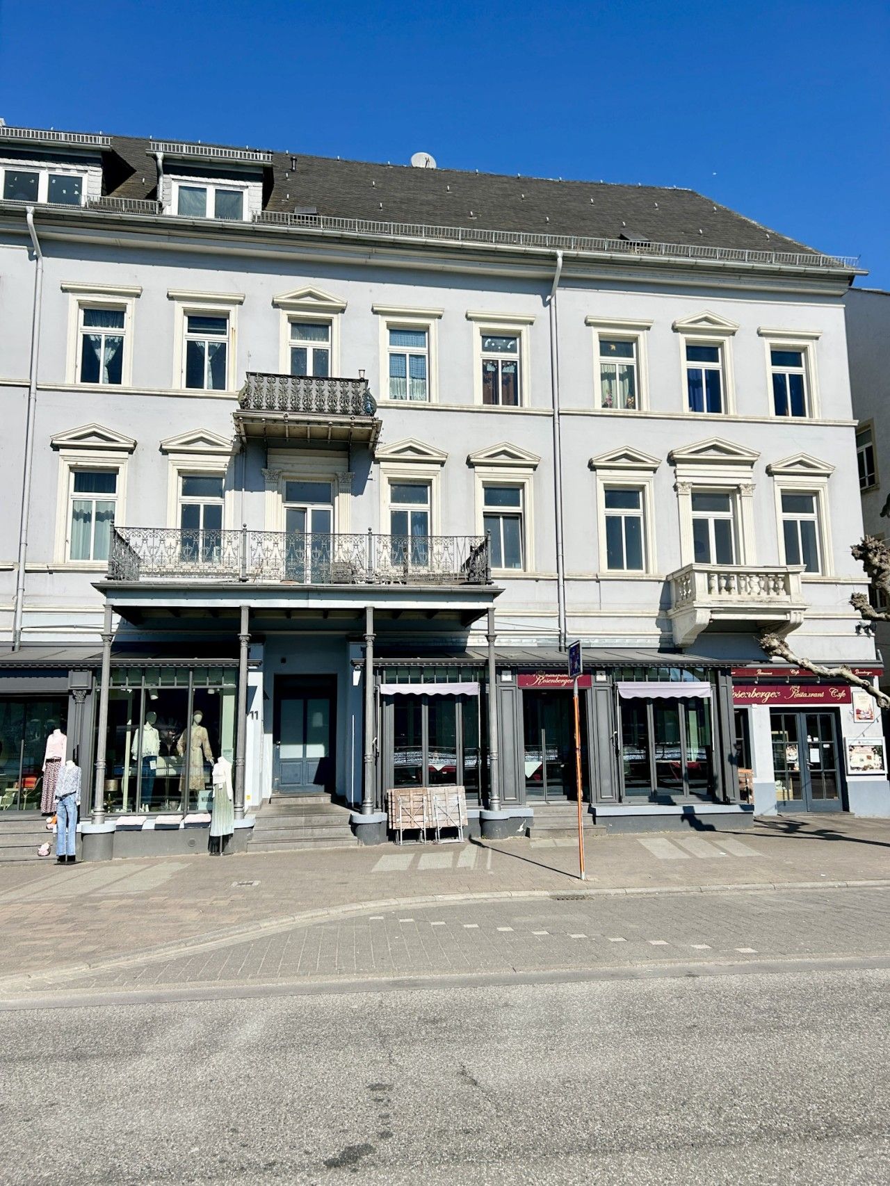 En byggnad med flera våningar, en central entré, stora fönster och en balkong på andra våningen.