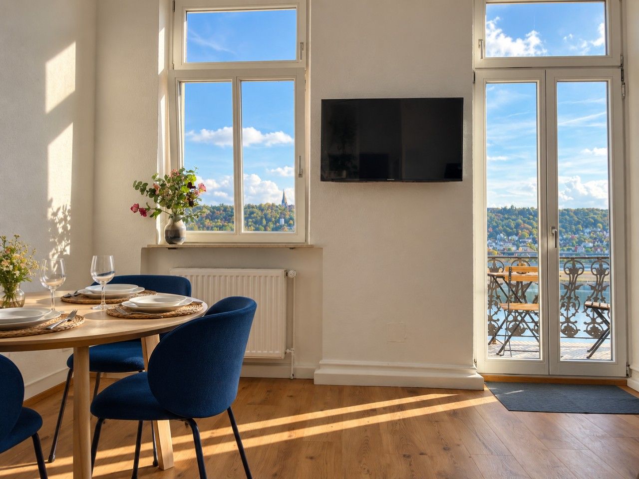 Ein Essbereich mit einem Tisch für zwei Personen, einem blauen Stuhl, einem Heizkörper und einem Fenster mit Blick auf eine Landschaft.