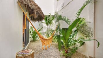 A narrow outdoor corridor with a hammock, potted plants, and a glass table.