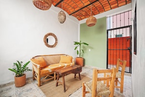 Habitació amb un sofà de vimet, una taula de fusta, cadires, una planta en test i un llum penjant.
