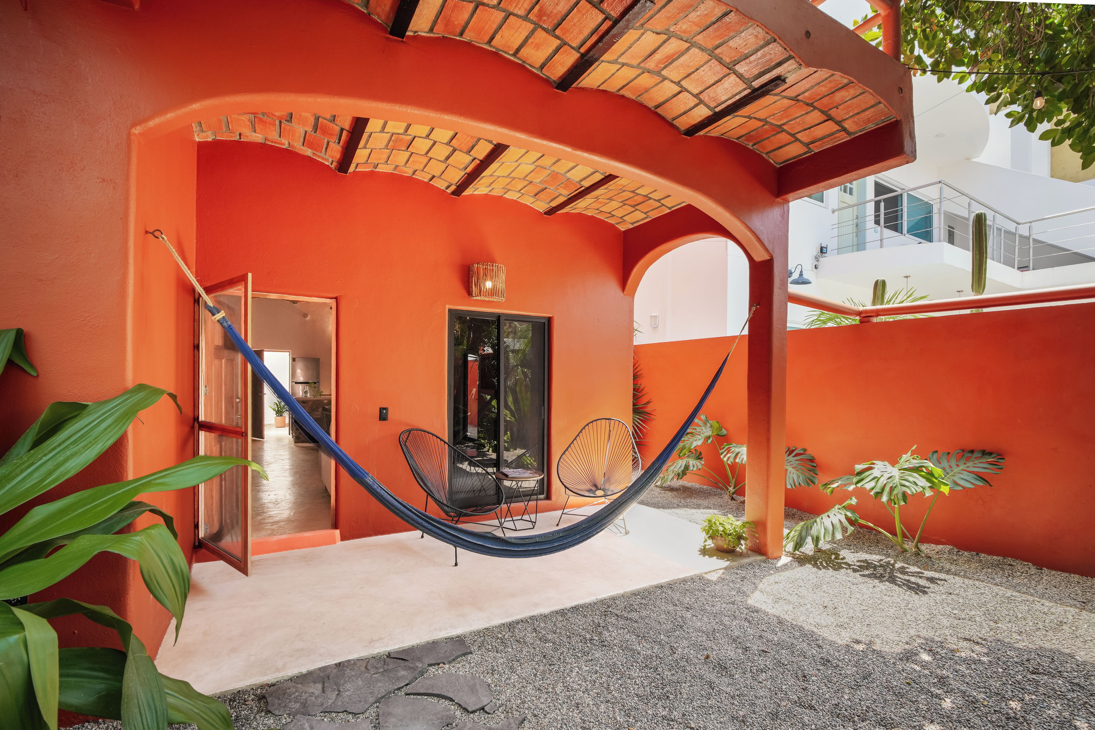 A red building with a hammock, a black chair, and a door leading to an interior space.
