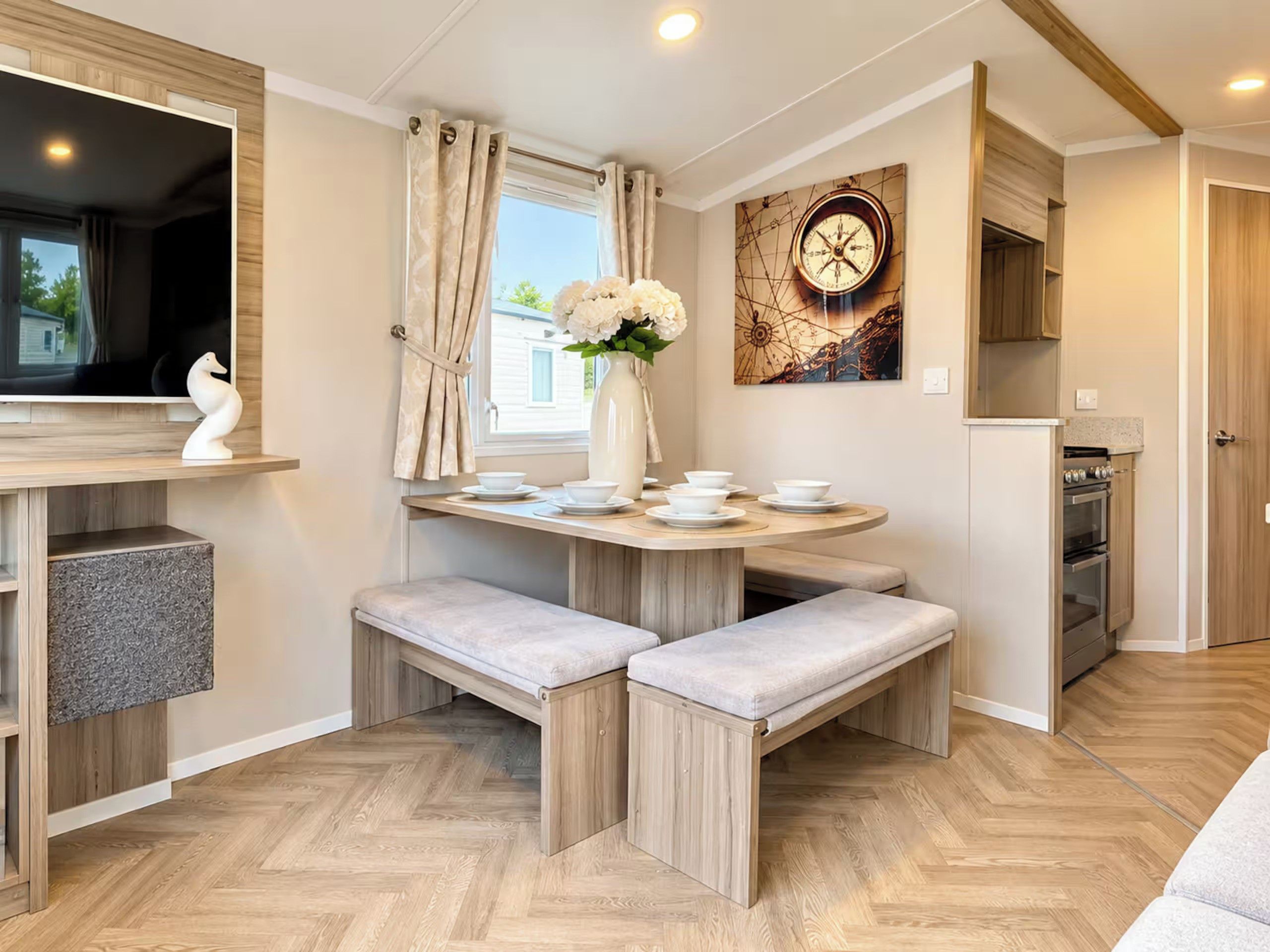 A compact kitchen with a dining area, a clock on the wall, and a window with curtains.