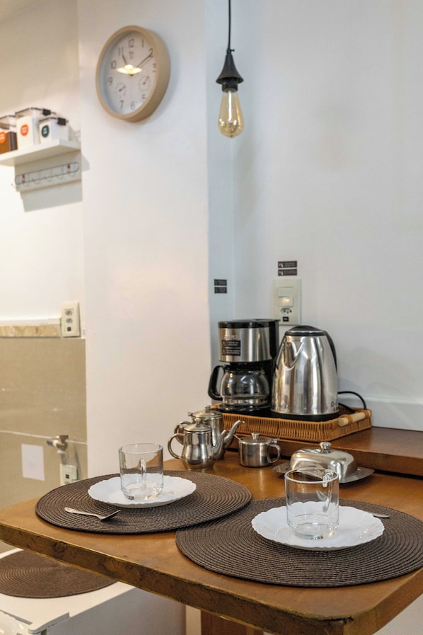 Un comedor con una mesa de madera, dos platos, un vaso, una tetera y una cafetera.