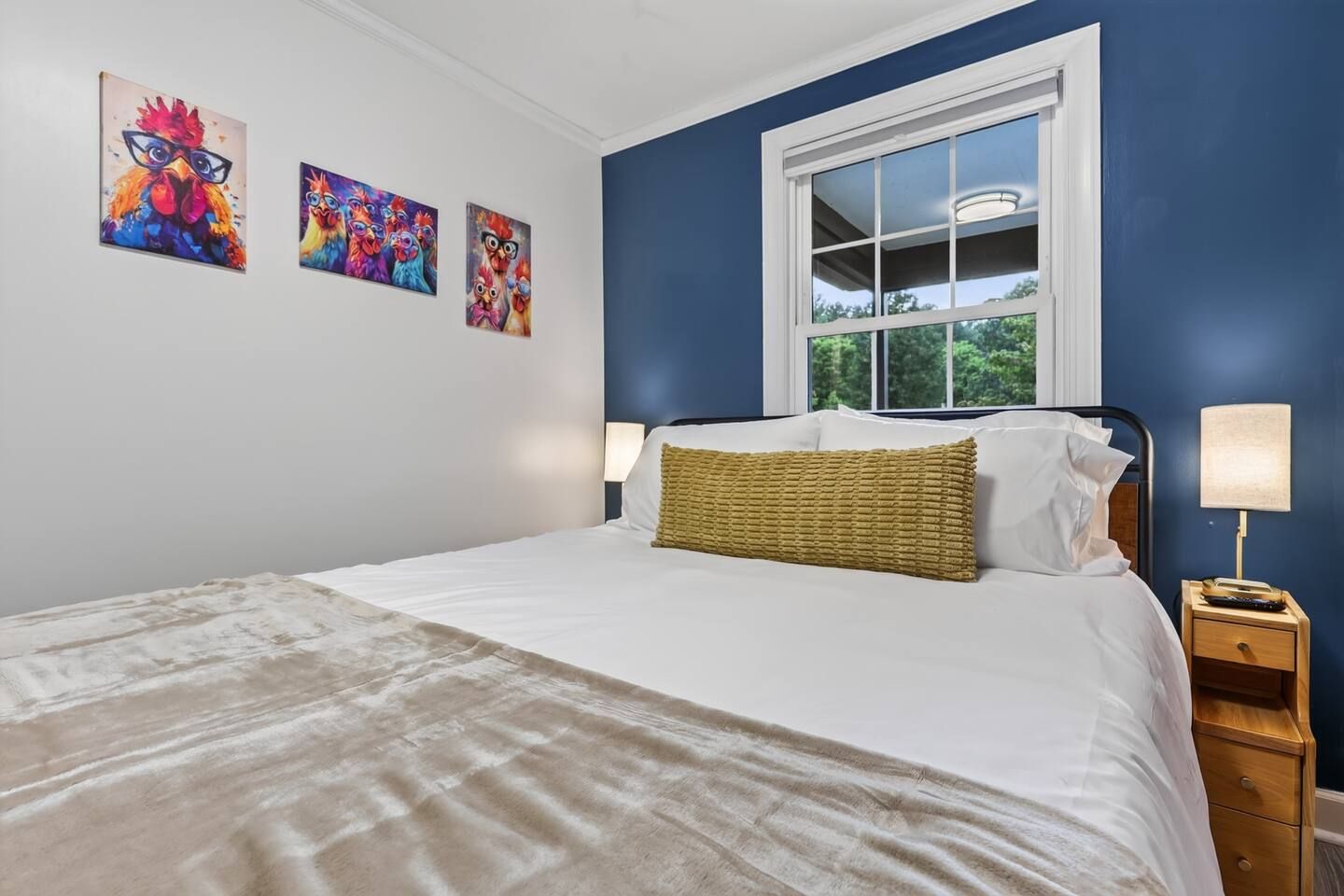A bedroom with a bed, a window, and three wall-mounted paintings.