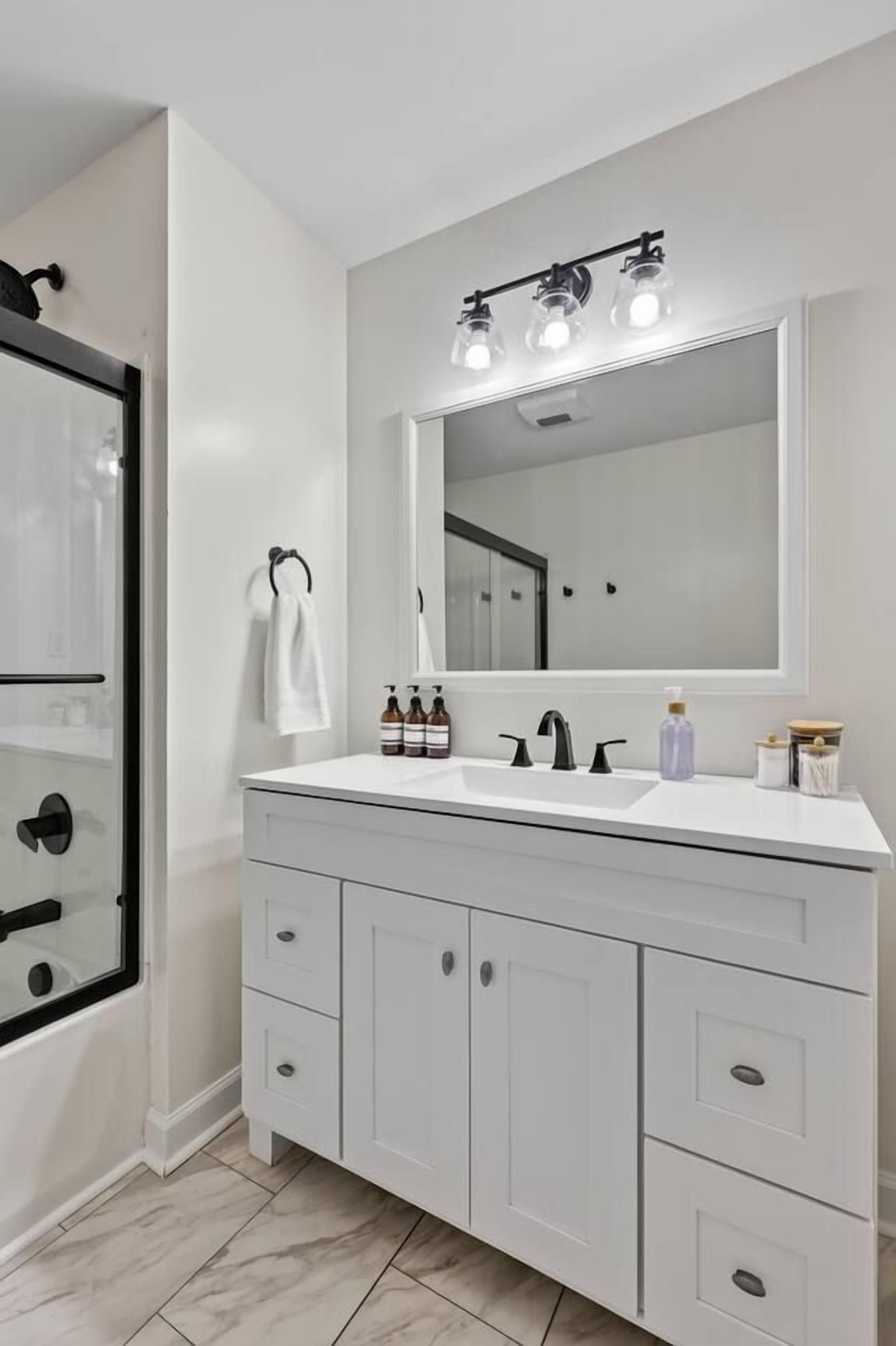 A modern bathroom with a white vanity, a large mirror, and a glass shower enclosure.