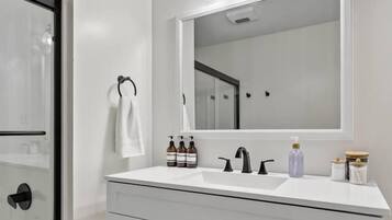 A modern bathroom with a white vanity, a large mirror, and a glass shower enclosure.