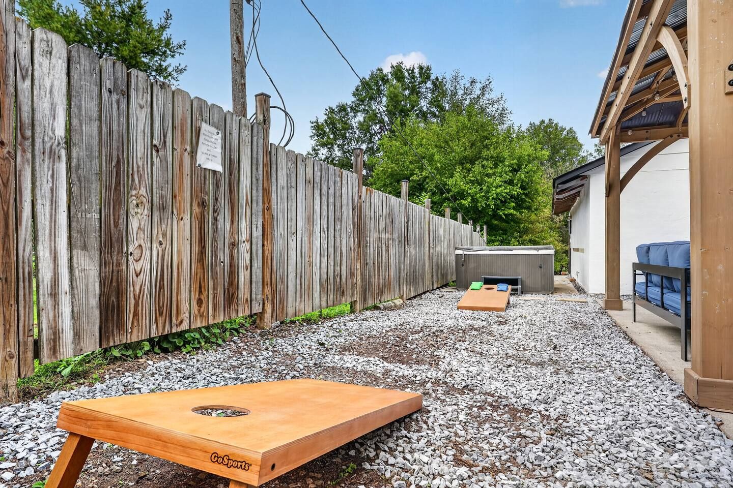 A backyard with a wooden fence, a gravel path, a wooden table, and a covered seating area.