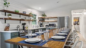 A modern kitchen with a long dining table set for six, equipped with a microwave, stove, and various utensils.