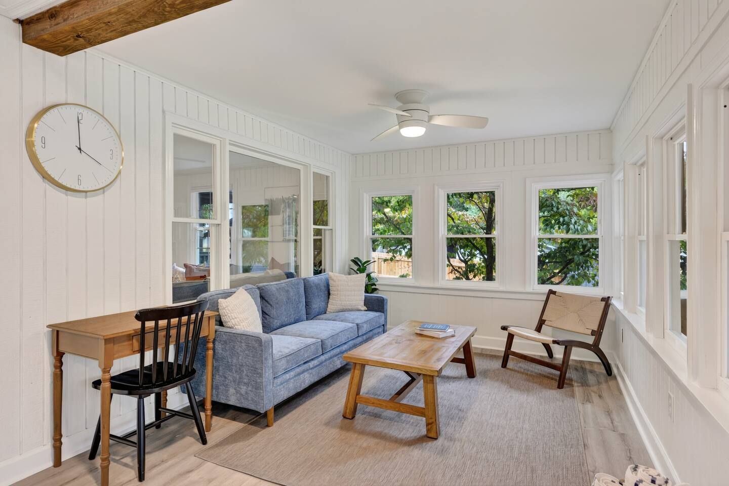 A room with a wooden table, a blue sofa, a wooden chair, and a clock on the wall.