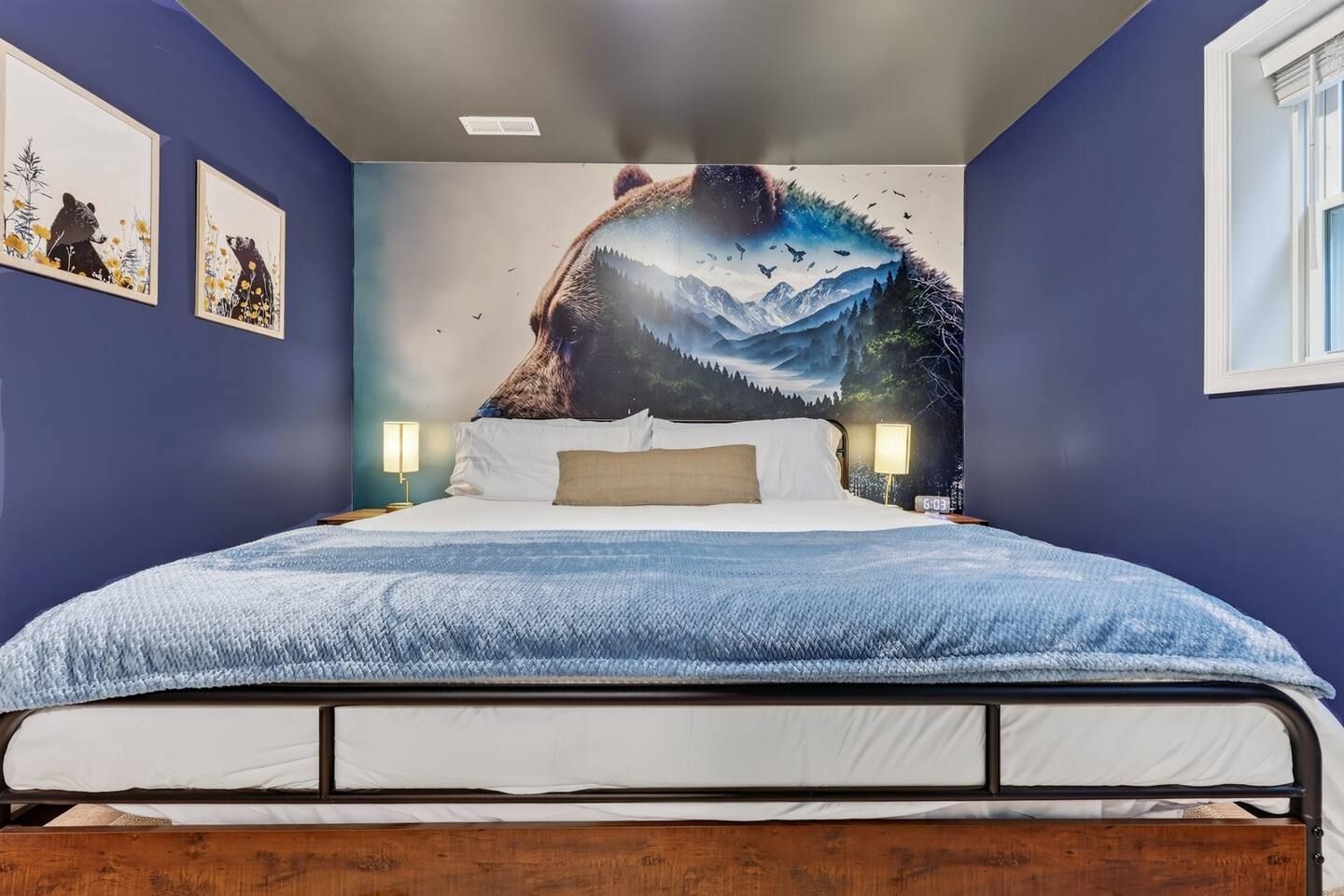 A bedroom with a bed, a wall mural, two bedside lamps, and a window.