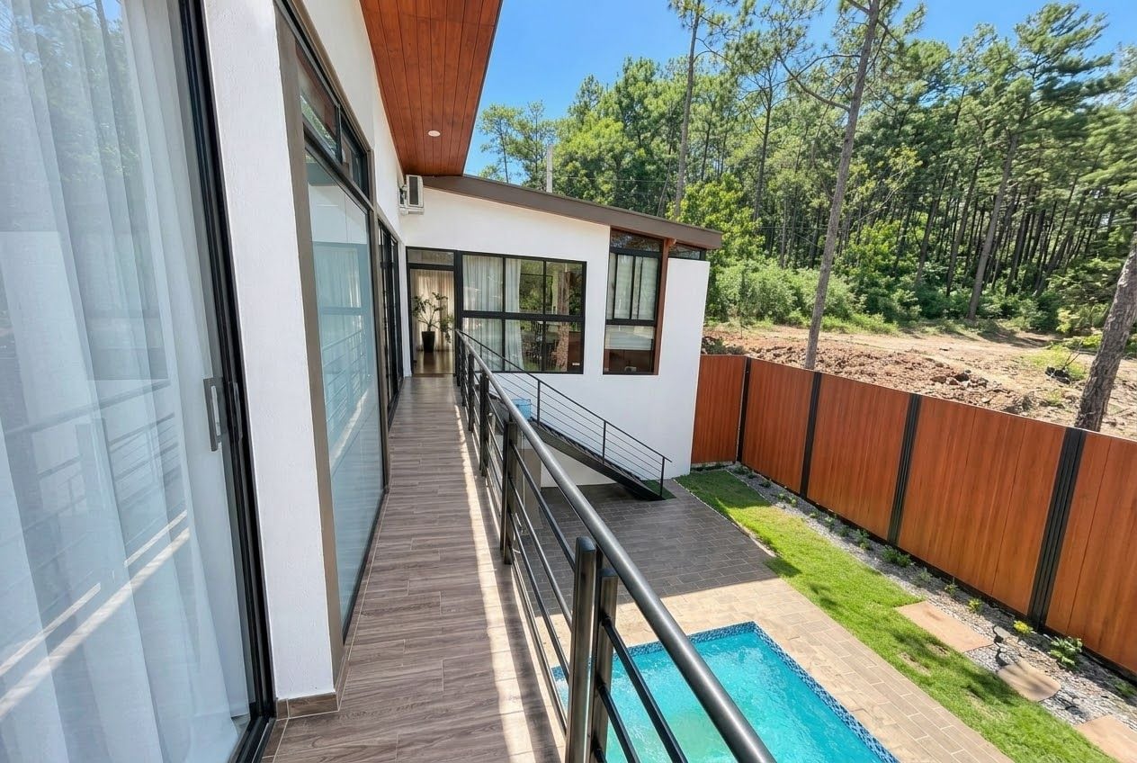 A modern house with a balcony overlooking a swimming pool and a forested area.