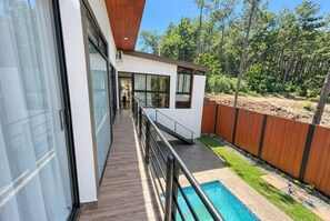 Una casa moderna con balcón que da a una piscina y un área boscosa.