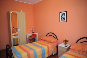Una habitación con cama, escritorio, silla, armario y mesita de noche con una planta.