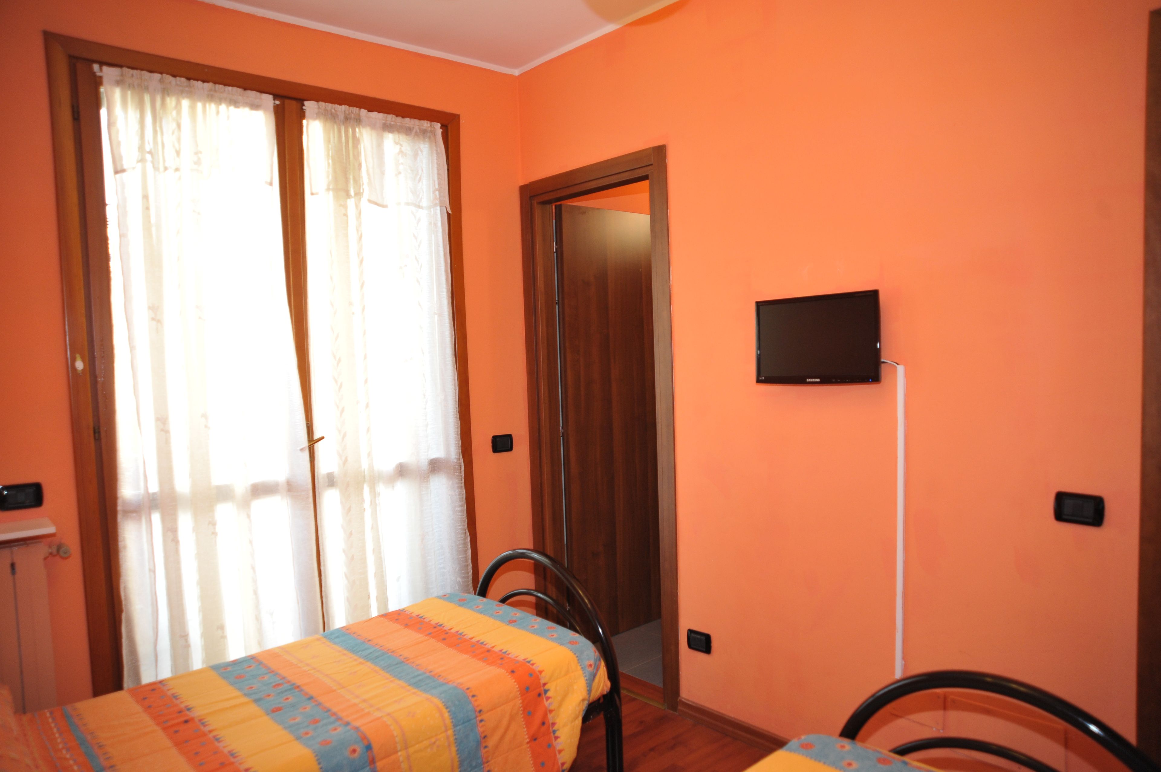 Una stanza con un letto, una sedia, una televisione a muro e una porta.