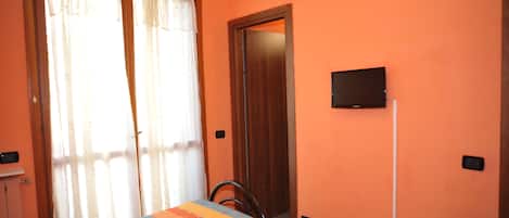A room with a bed, a chair, a television mounted on the wall, and a door.