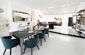 Un comedor moderno con una mesa de vidrio, sillas color turquesa y piso de baldosas blancas.