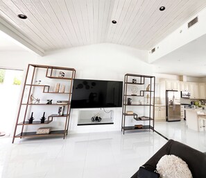 Amplia sala de estar con una gran televisión de pantalla plana, estanterías de madera y una cocina moderna al fondo.