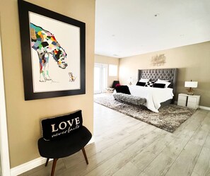 Un dormitorio moderno con una cama grande, una obra de arte enmarcada en la pared y una silla negra con cojín.