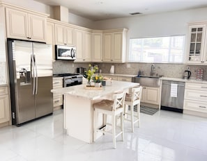 A modern kitchen with white cabinetry, stainless steel appliances, a marble countertop, and a central island with bar stools. - Resort Style Compound with detached Casita & Pool (Los Angeles)