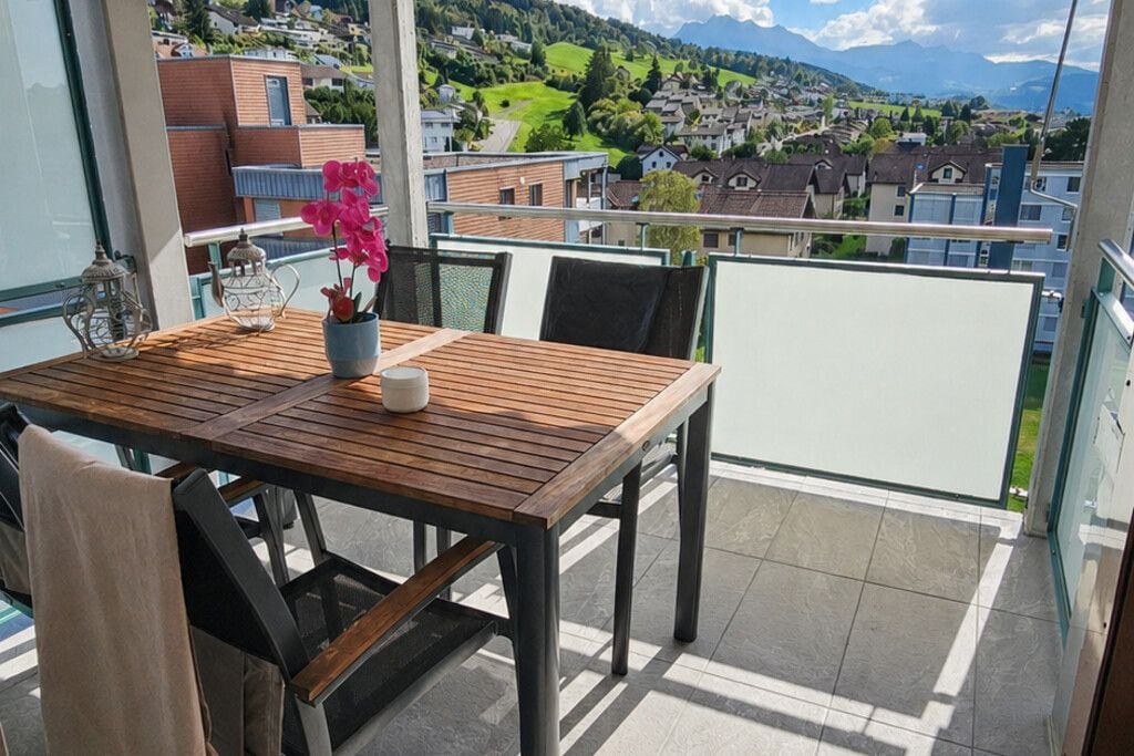 Un balcon avec une table en bois, des chaises et un pot de fleurs.