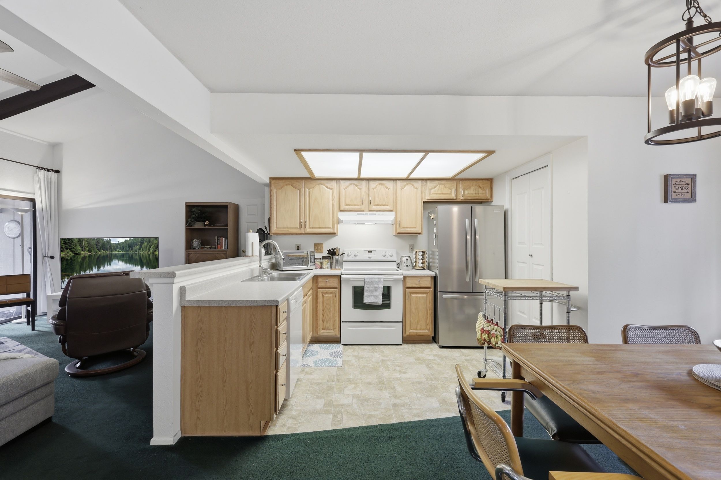 A modern kitchen with a central island, wooden cabinets, stainless steel appliances, and a dining area with a wooden table and chairs.