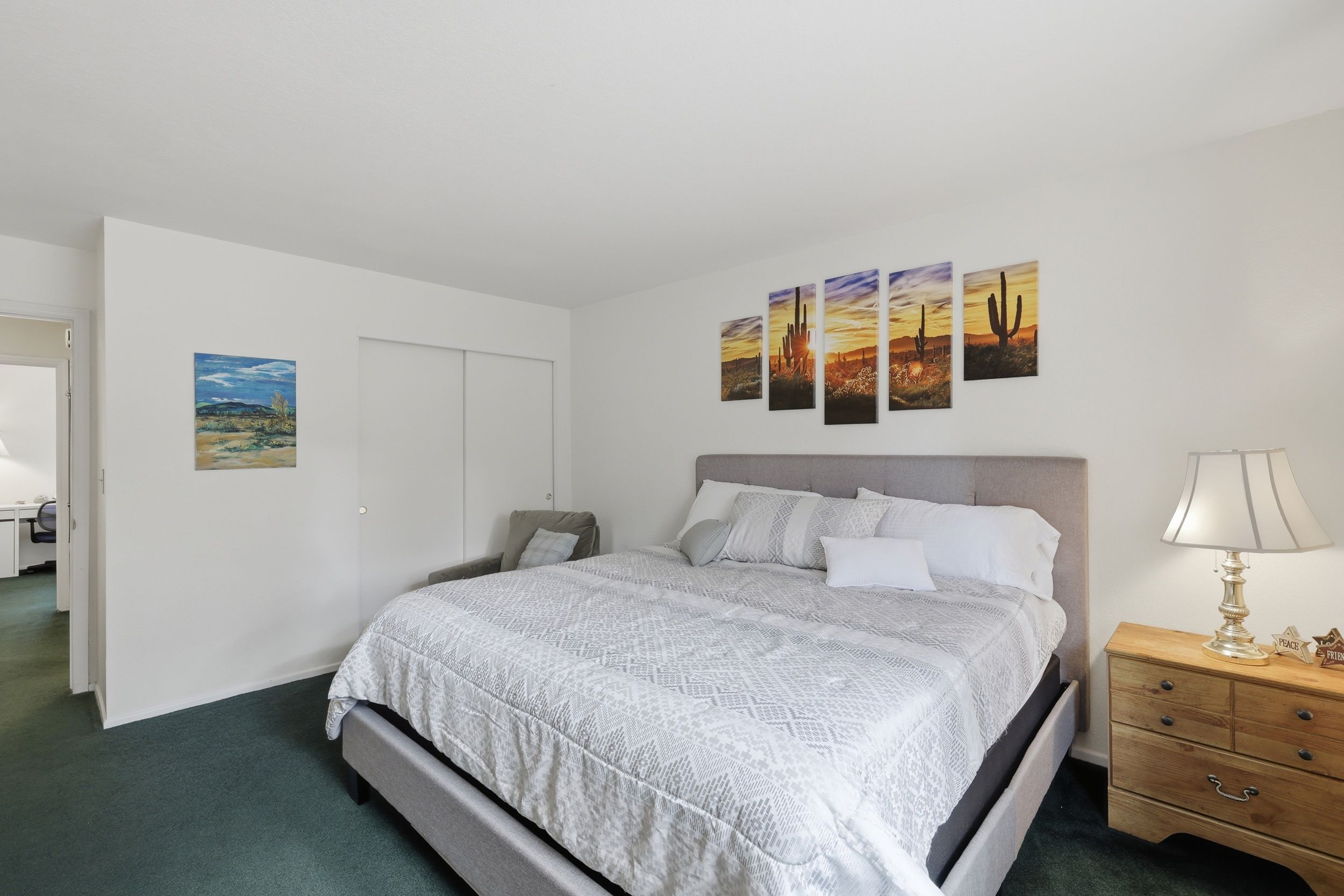 A bedroom with a bed, a nightstand, a lamp, and a wall with paintings.