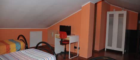 A room with two beds, a desk with a chair, a wardrobe, and a door.