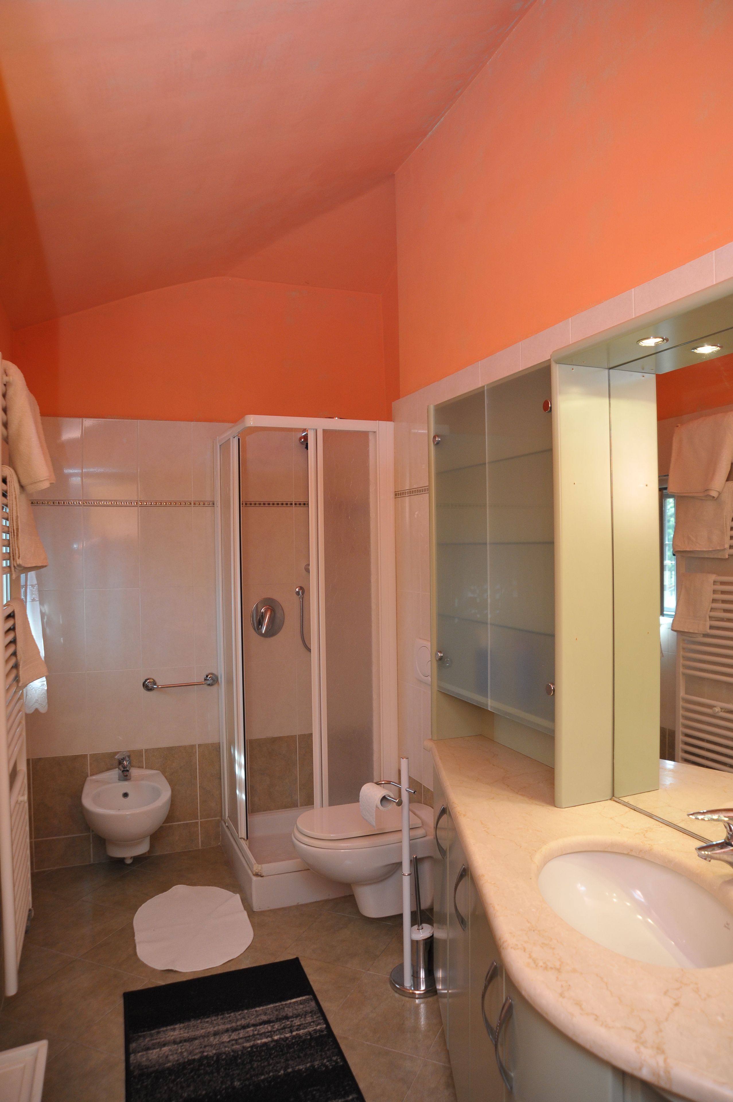 Un bagno con doccia vetrata, un bidet, un water e un lavandino con specchio sopra.
