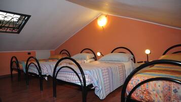 A dormitory room with four beds, each with a headboard and a bedside lamp.