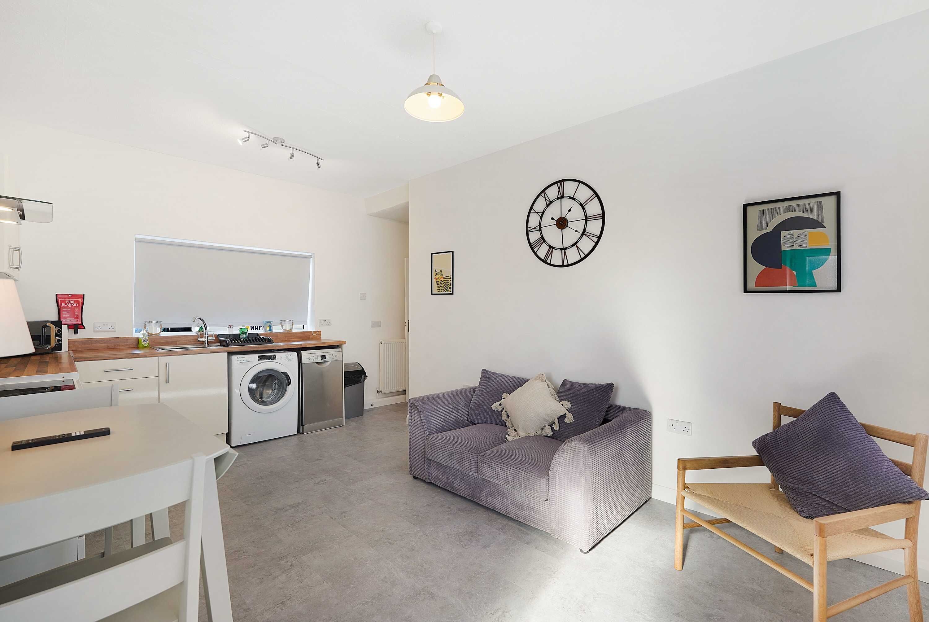 A modern living space with a kitchen, a dining area, and a seating area with a sofa and a chair.