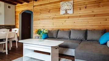 A modern living room with a white coffee table, grey sofa, and a wooden wall with a tree artwork.