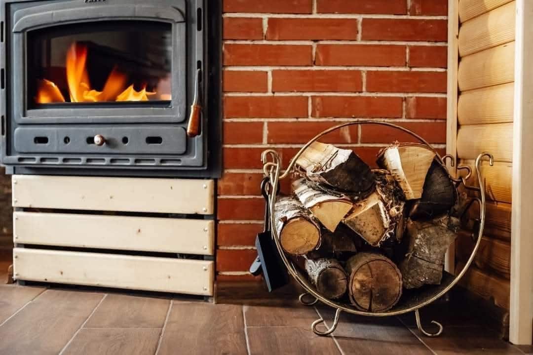 A wood-burning stove with logs in front of a brick wall.