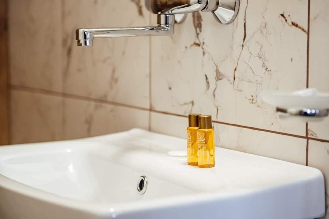 A bathroom sink with a chrome faucet, a marble wall, and a soap dispenser.